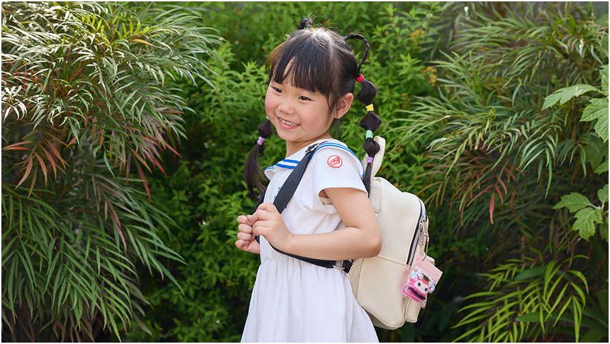 緑の植物の前でバックパックを背負った笑顔の少女