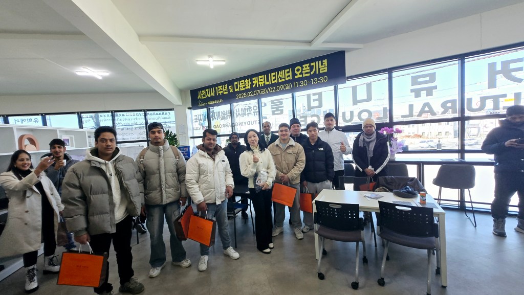 コミュニティセンターのオープニングイベントに参加しているグループの写真。参加者たちはカメラに向かって微笑んでおり、オレンジのバッグを持っている。