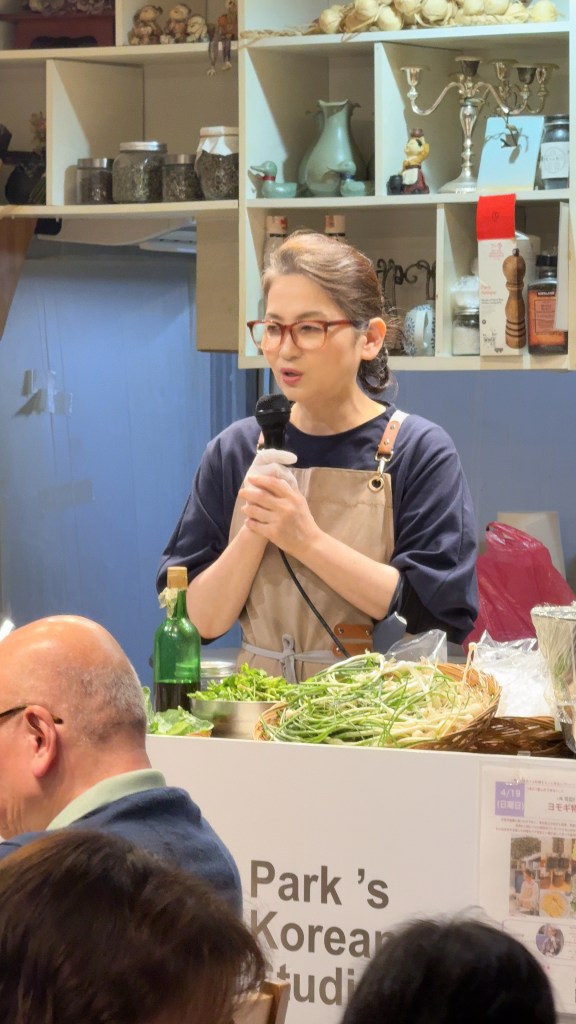 料理教室で話している女性インストラクターと、その背景にある韓国の食材や装飾品が描かれたシーン