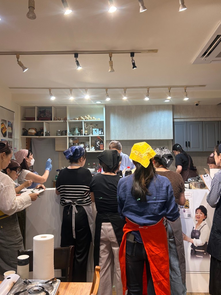 調理教室で参加者が料理を作る様子。シェフに向かっている人々がキッチンで作業している。