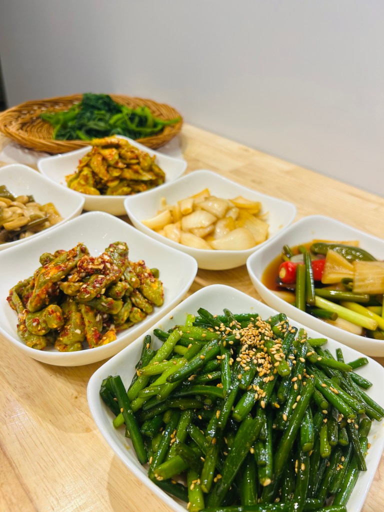 様々な韓国風の副菜が並んでいる食卓の写真。小皿には緑の野菜や漬物、和え物が盛り付けられている。