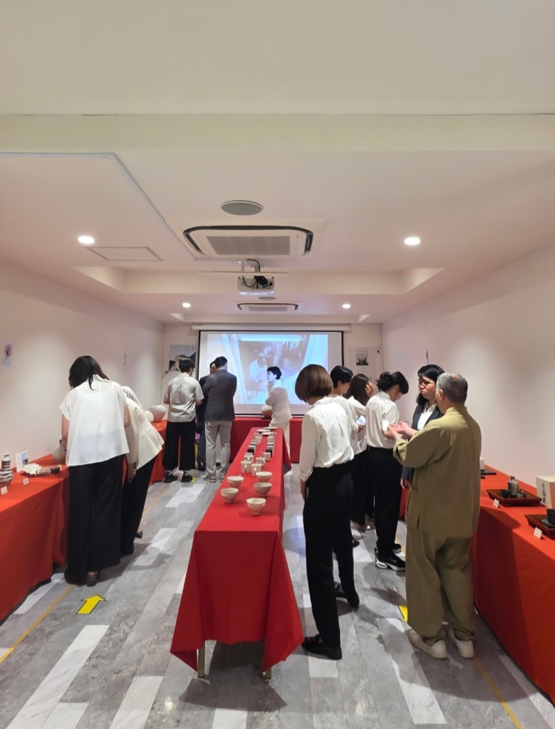 赤いテーブルの周りで会話する人々、後方にプロジェクター画面がある