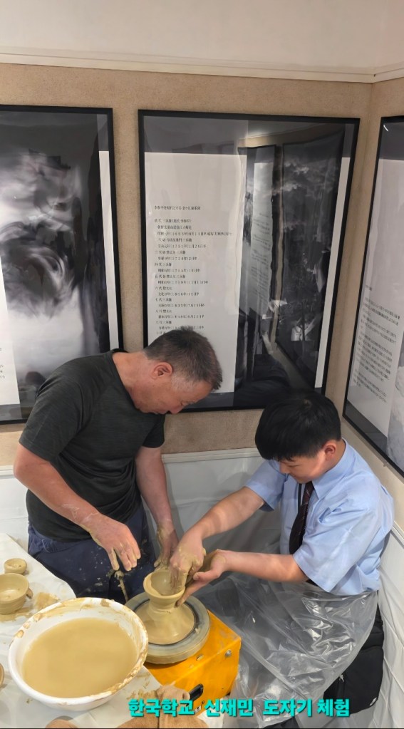 陶芸を学ぶ二人の男性。手を使って陶器を形作っている様子。背景には展示パネルが見える。