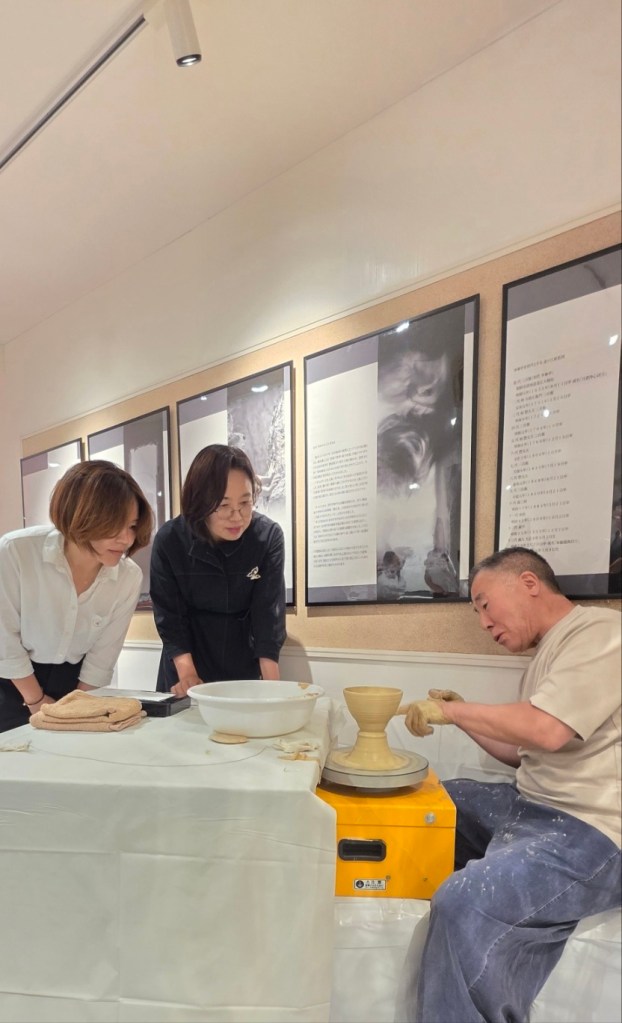 陶芸のデモンストレーションを見守る二人の女性と作業する男性